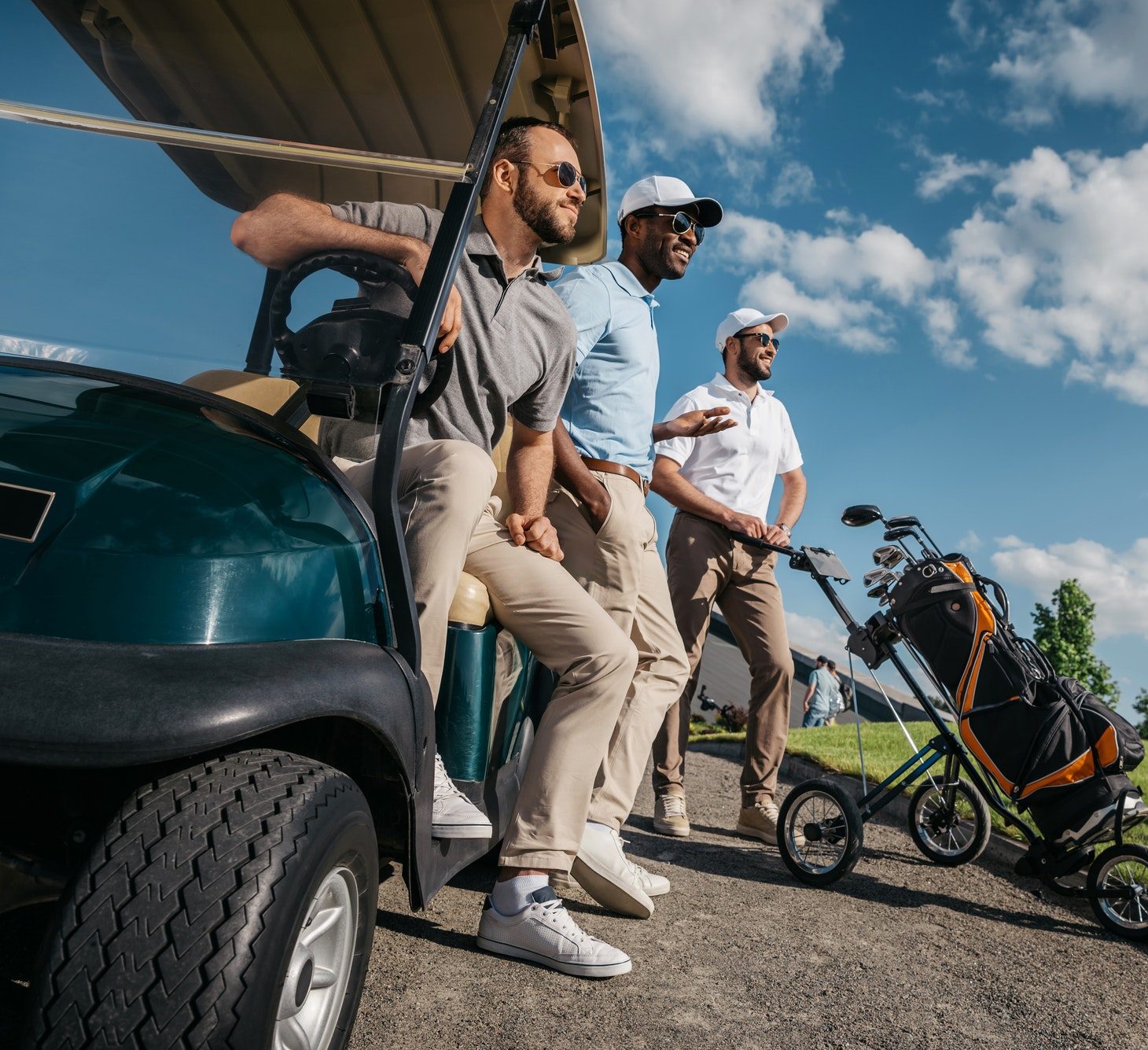 Grupo de amigos sonrientes junto a un carrito de golf en un campo, disfrutando de una experiencia social y deportiva
